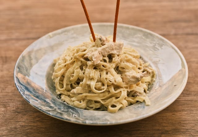 Creamy chicken fettuccine alfredo pasta served in a ceramic bowl on a rustic wooden table.