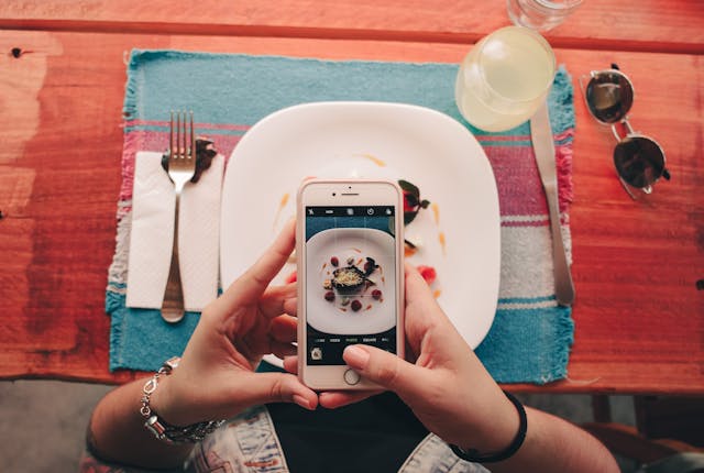 a person holding a cell phone in front of a plate, thinking of tips to write compelling captions
