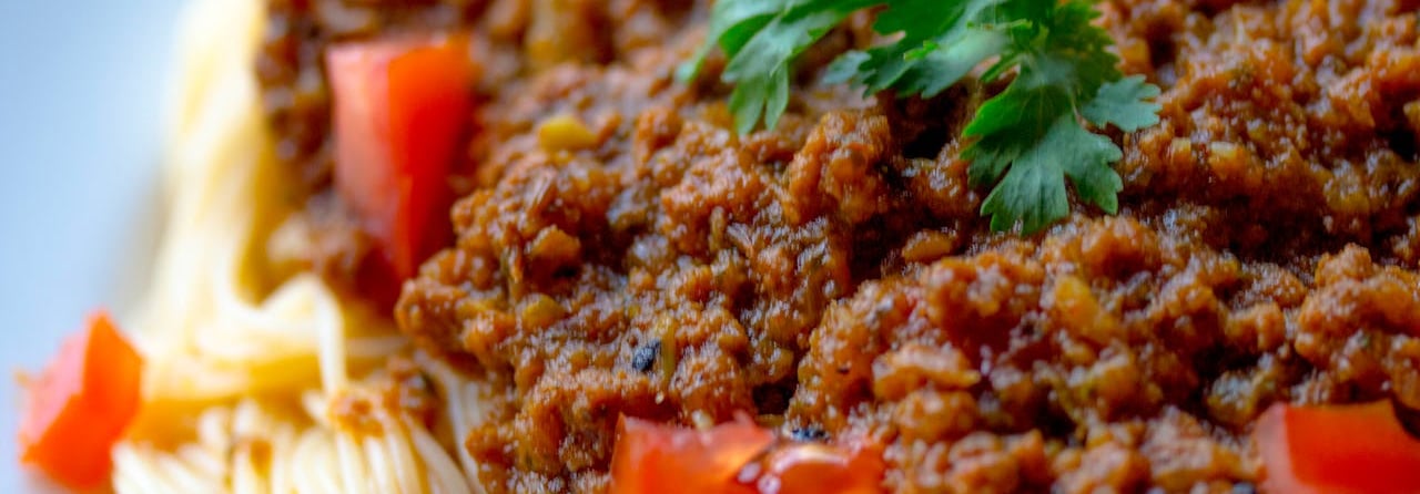 A close-up of spaghetti bolognese topped with fresh diced tomatoes and a sprig of parsley.