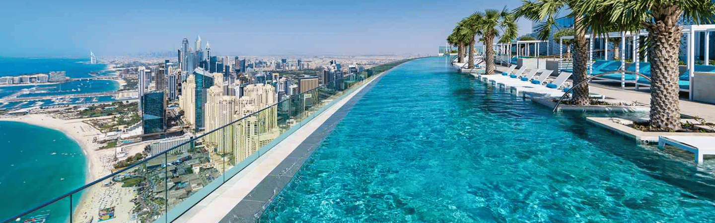 Rooftop infinity pool with clear turquoise water and pale mosaic tiles stretching toward the skyline
