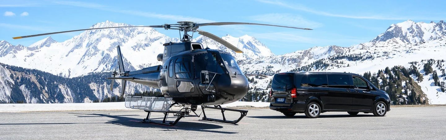 As350 helicopter with Mercedez Benz V-Class VIP vehicle on a helipad, with snowy mountains behind.