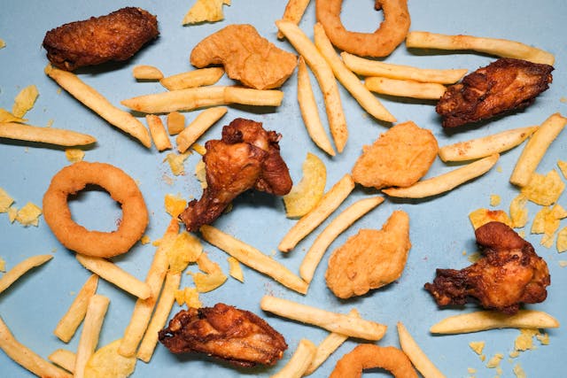 Flat lay of crispy fried chicken wings, chicken nuggets, french fries, and onion rings on a blue background.