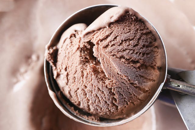 A metal scoop picking up a textured scoop of creamy gourmet chocolate ice cream.