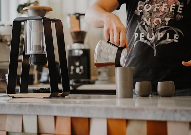 Barista pouring specialty drip coffee from a glass carafe into a ceramic mug, coffee brewing methods