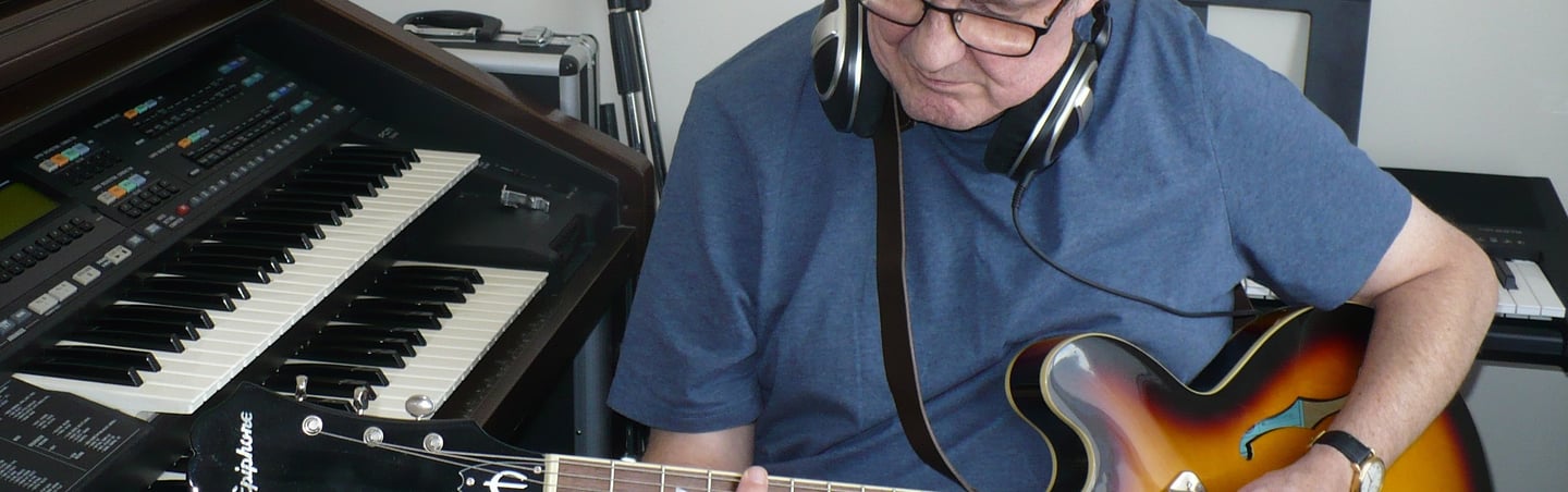 photograph of Julian Sumner with guitar and keyboards in recording studio