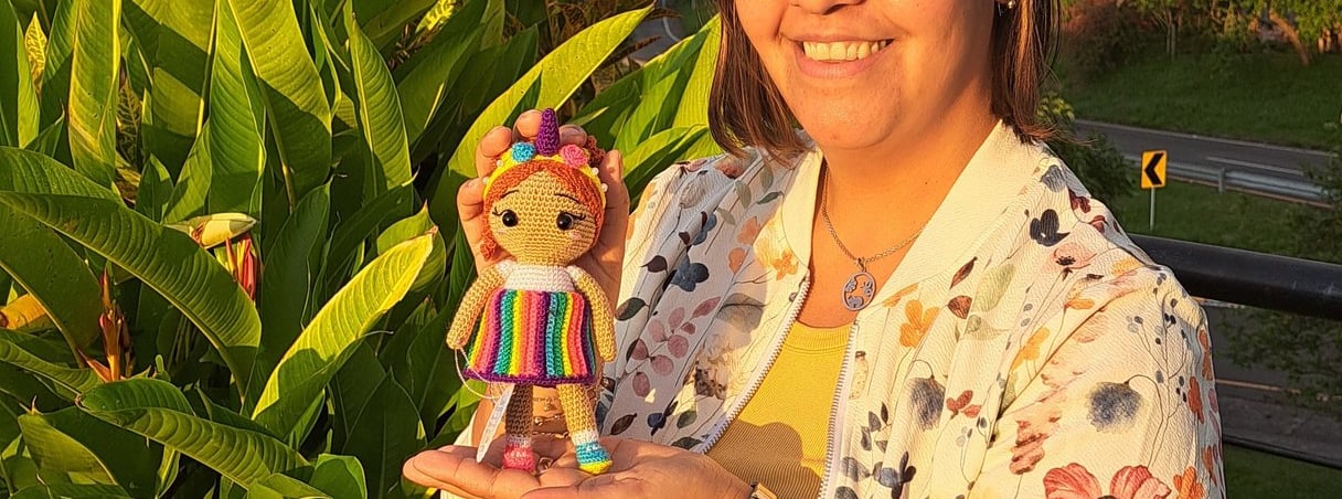 Una persona sonriendo sosteniendo un amigurumi con un vestido multicolor