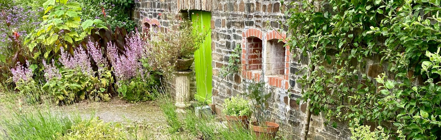 Rustic stone garden wall with a bright green wooden door, potted plants, and blooming lavender.