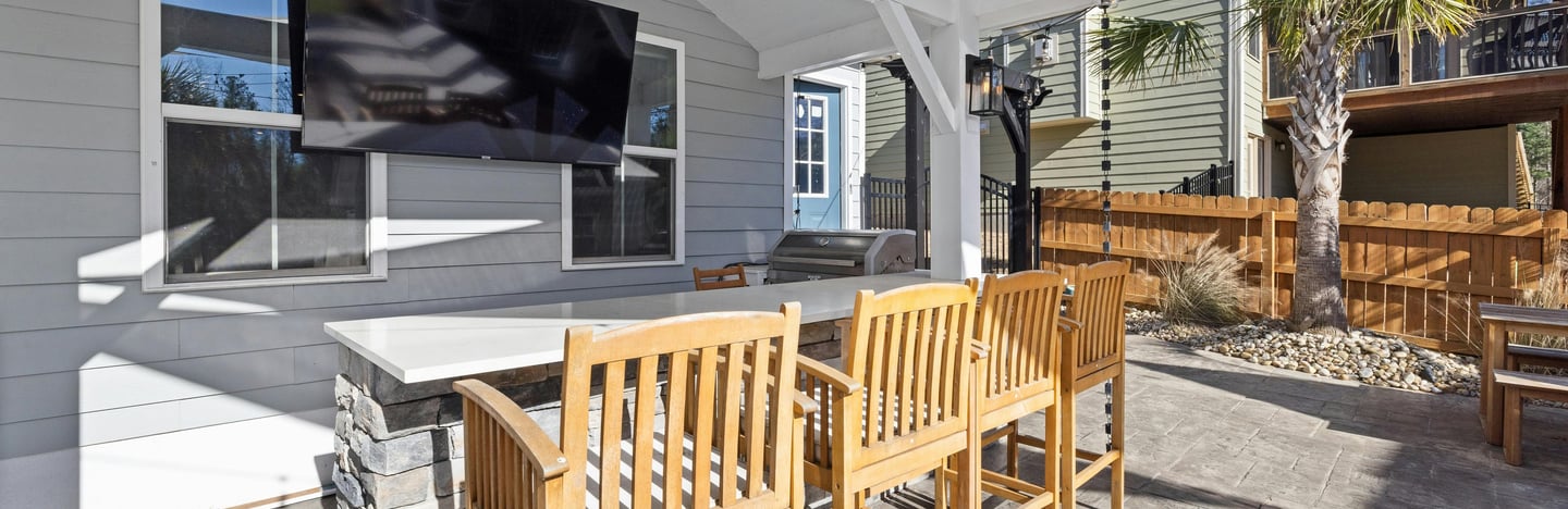 Covered outdoor bar area with wooden bar stools, a mounted TV, stone counter,