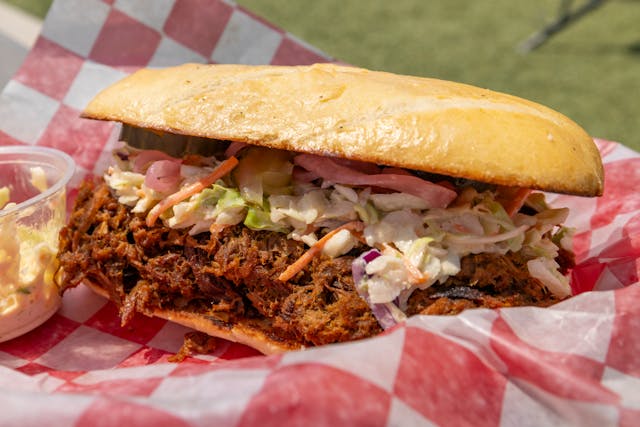 Pulled beef sandwich topped with creamy coleslaw on a toasted bun in a red checkered basket.