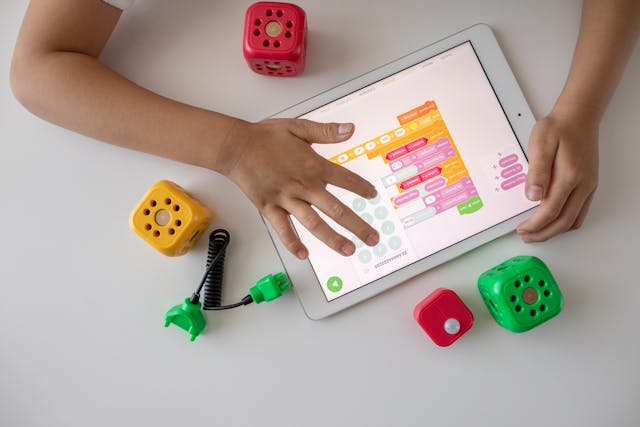 A child uses a tablet for visual coding with colorful STEM blocks and educational toys.