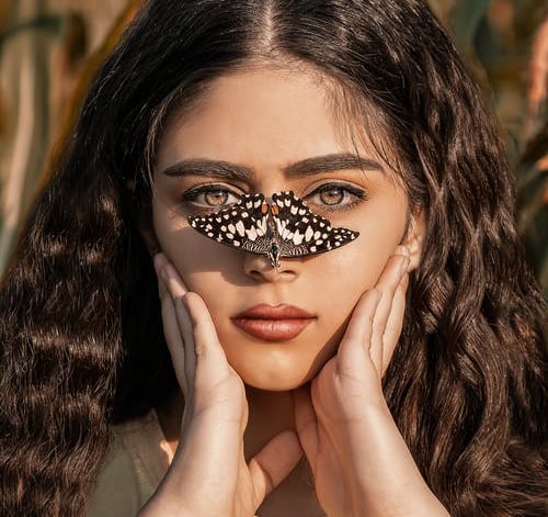 spanish lady holdung fase with 2 hands and butterfly lend on her nose