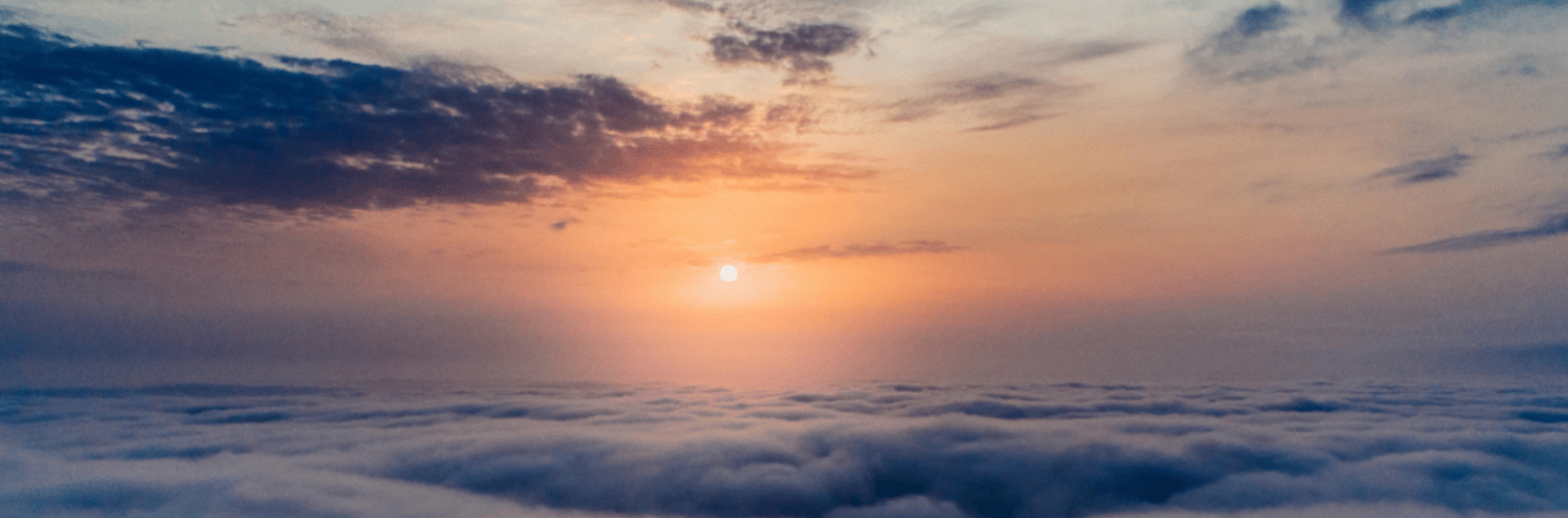 Panoramic aerial view of a golden sunrise over a thick layer of white clouds and a soft blue sky.