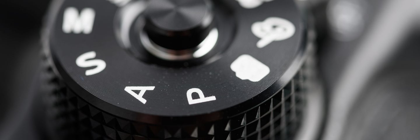 Close-up of a DSLR camera mode dial showing Auto (A), Program (P), settings, symbolising the choice between auto and manual