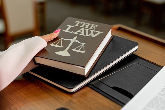 A person holding a brown book titled The Law with scales of justice on a courtroom desk.
