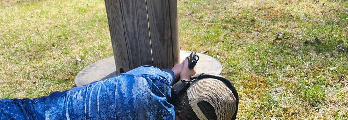 Man laying on side engaging targets from a barrier using self-defense firearm during training.