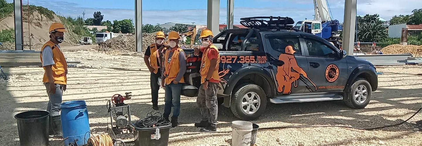 Professional termite control team with equipment and service truck at a construction site.