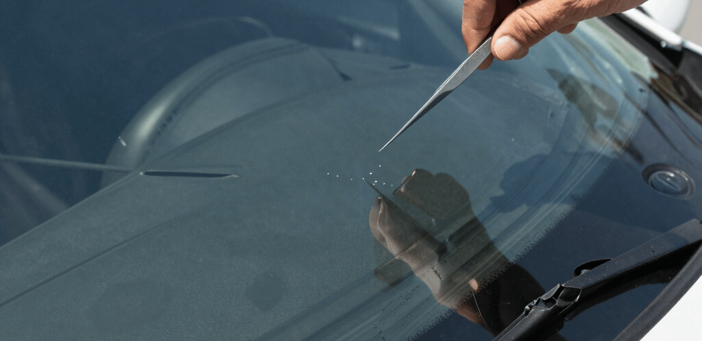 A friendly technician repairing a small windshield chip under bright Southern California sunlight.