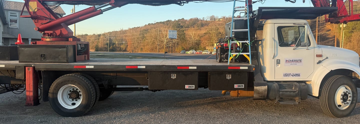 White Oversite boom truck with a red crane and flatbed parked in a gravel lot.