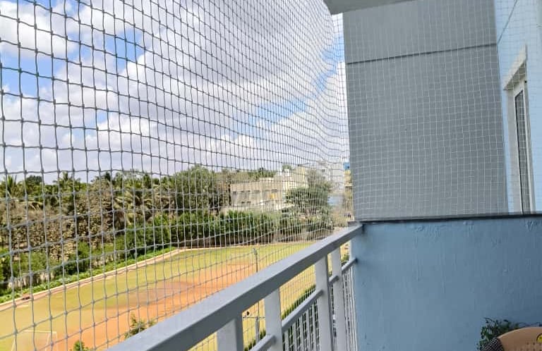 A technician carefully installing a sturdy balcony net on a sunny Chennai apartment balcony.