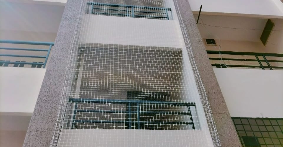 A technician carefully installing a safety net on an apartment duct in Velacherry.