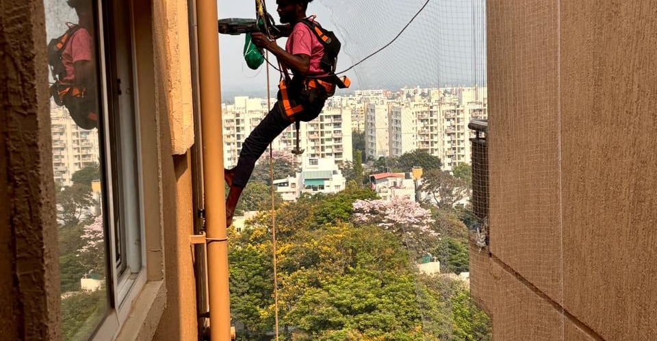 A friendly technician installing a balcony safety net on a sunny day in Ahmedabad.