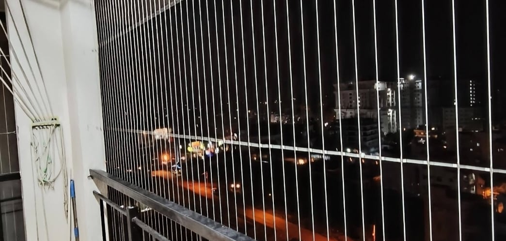 A technician carefully installing a balcony safety net on a sunny day in Kolathur, Chennai.