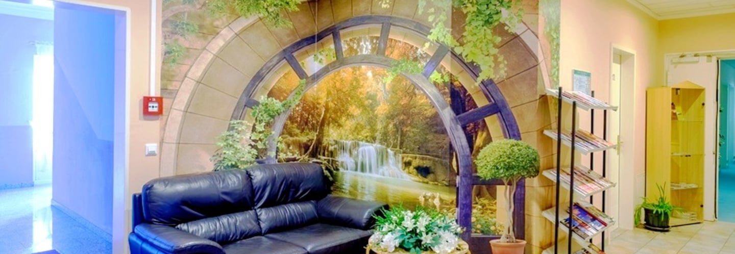 A waiting area with a black leather sofa and a nature wall mural featuring a waterfall and forest.