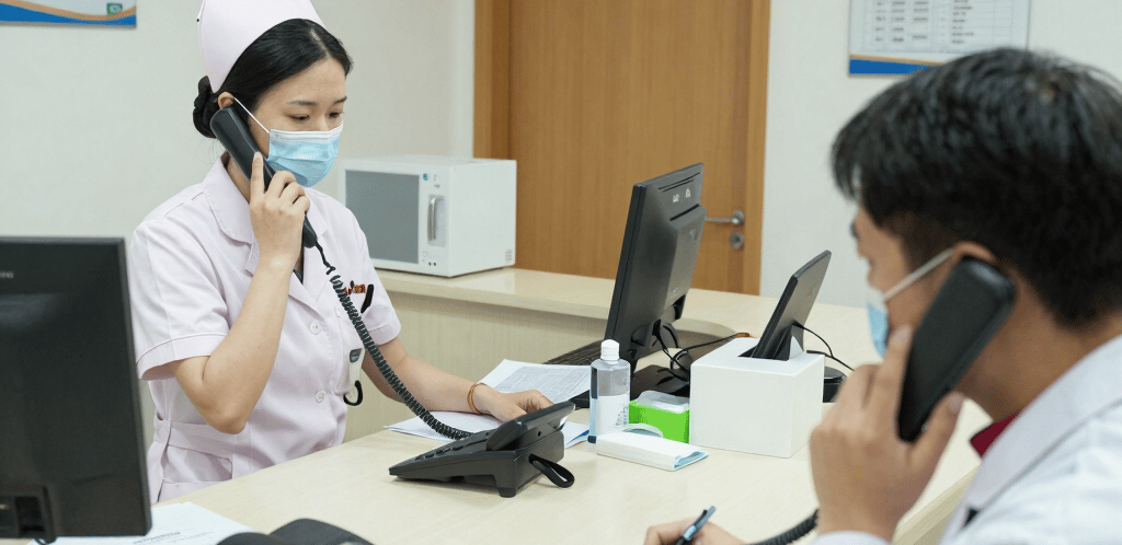 A friendly automotive dealership receptionist speaking on a sleek phone system with car showroom in the background.