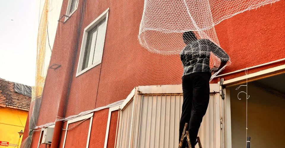 A technician carefully installing pigeon nets on a balcony in Hebbal under bright daylight.