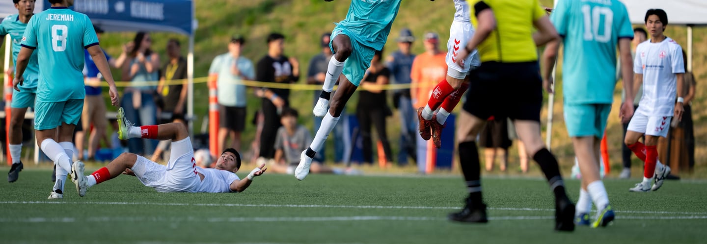 Soccer players in action, one is lying on the ground, two sets of feet leaping.
