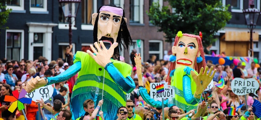 2 Giant puppets wearing yellow reflector vests used in the Amsterdam Pride one is covering mouth