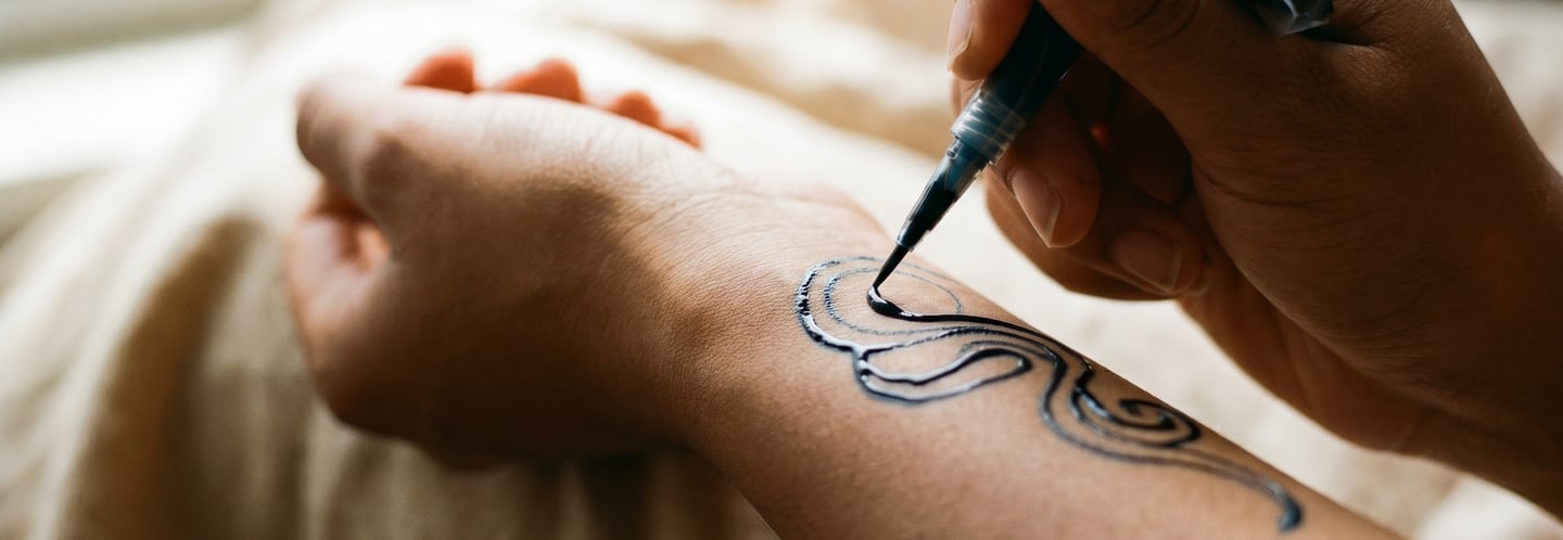 Close-up of a person applying a black henna ink temporary tattoo design to their forearm with an applicator.