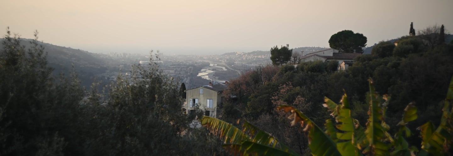 Panoramic view of a hillside village in Nice, France, overlooking the Var river valley at sunset.