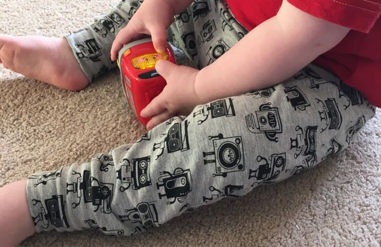 a toddler boy sitting on the floor with a toy wearing robot music robot themed leggings