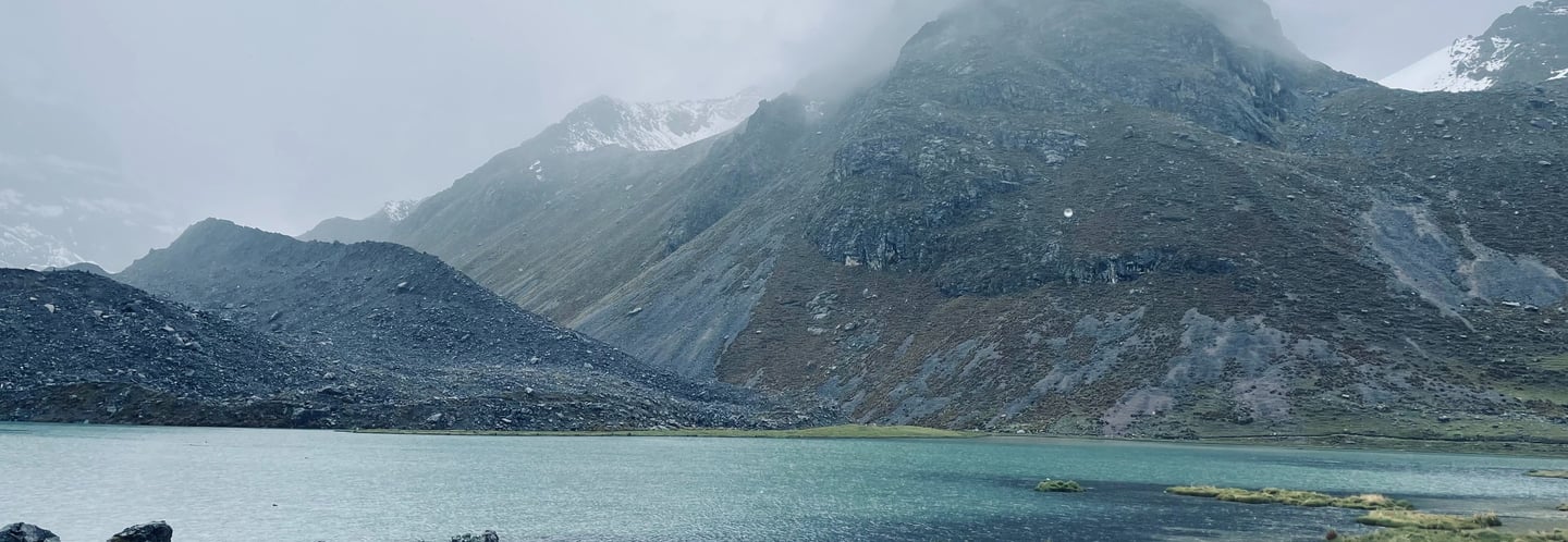 Misty mountain range in Peru overlooking a turquoise glacial lake in a rocky alpine landscape.
