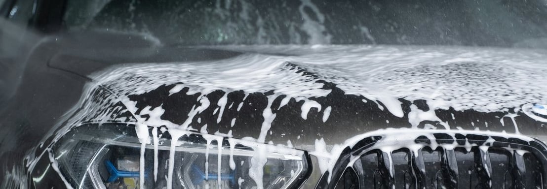 soapy front grill, lights and bumper of a grey bmw that is dripping wet with soap running down.