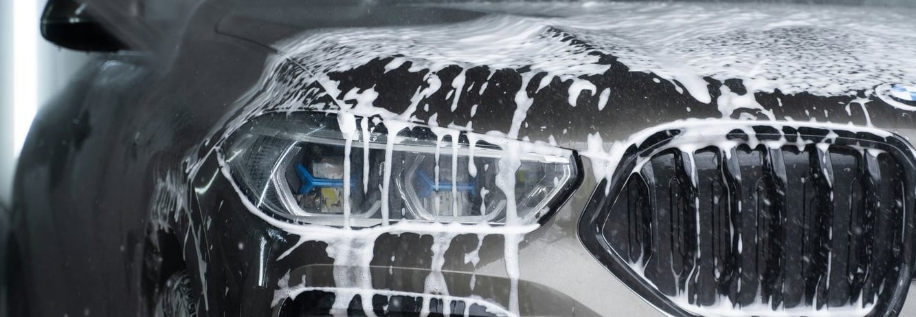 front grill, lights and bumper of a grey bmw that is  dripping wet with soap running down. 