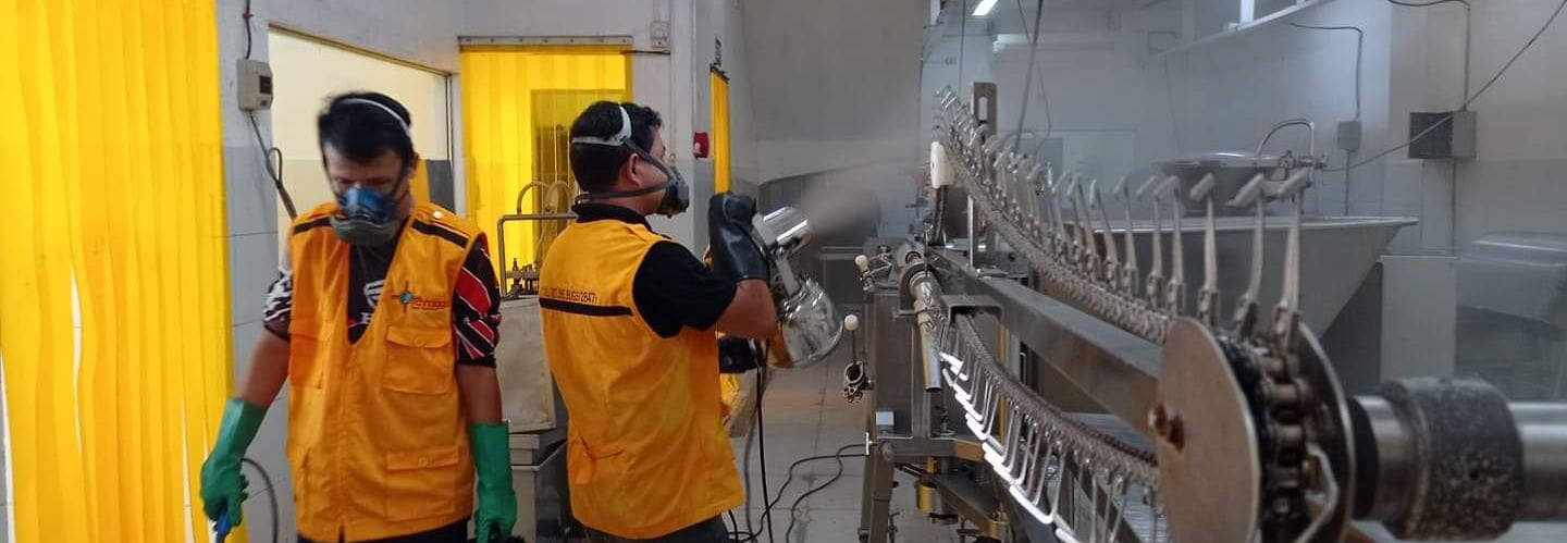 Sanitation workers in safety gear spray disinfectant on a commercial meat processing line for industrial hygiene.
