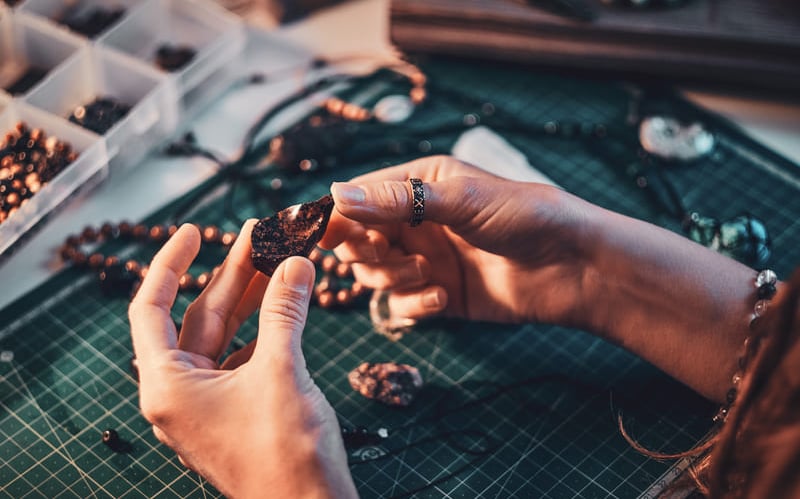  Manos de un joyero sosteniendo una piedra preciosa oscura en una mesa de taller con cuentas y herra