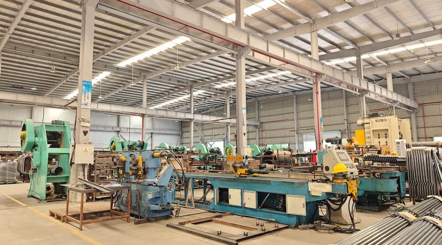 Industrial metal display racks workshop with heavy machinery and bundles of steel pipes.