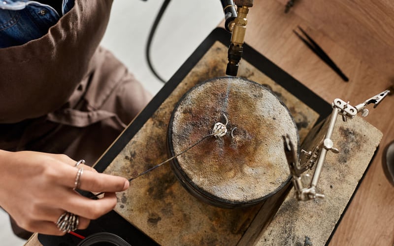 Joyero trabajando con un soplete sobre una pieza de metal en su mesa de trabajo