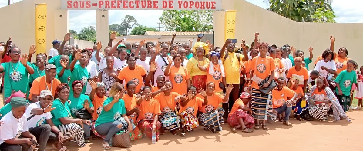 Community group in orange and green shirts posing at Sous-Prefecture de Yopohue in Gagnoa, Ivory Coast.