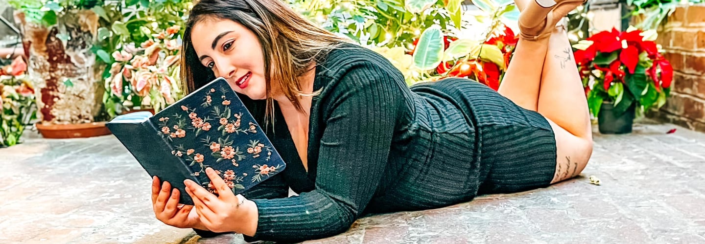 Patricia laying on the floor in a garden reading a journal