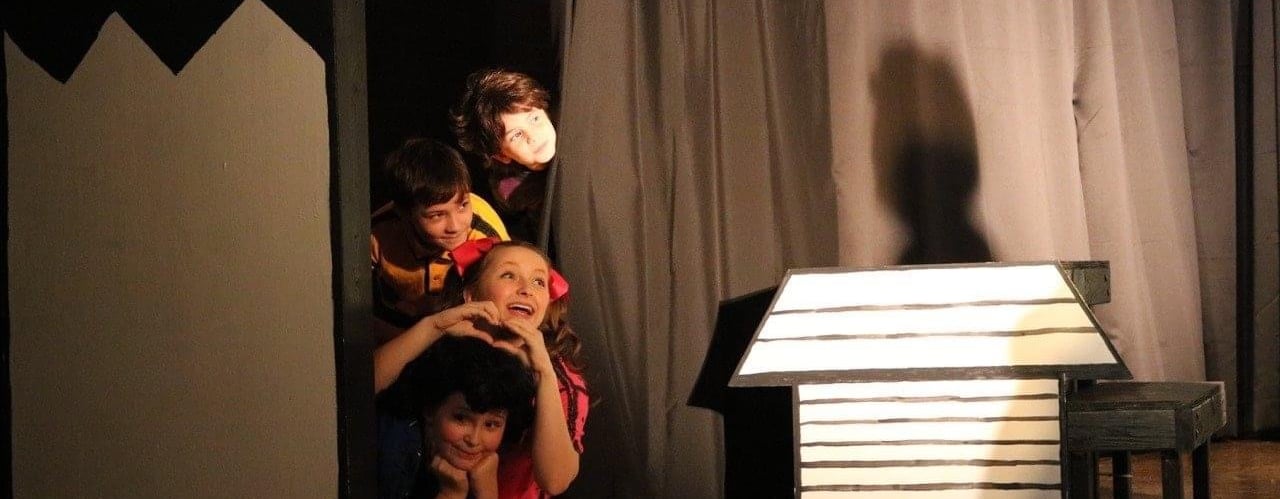 Young children performing a musical on stage in colorful costumes.