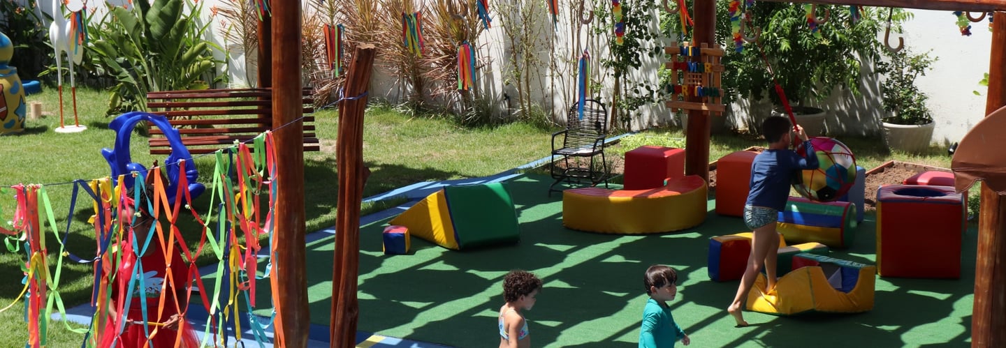 Espaço de brincadeiras com crianças brincando  com bola, e brinqueros acochoados