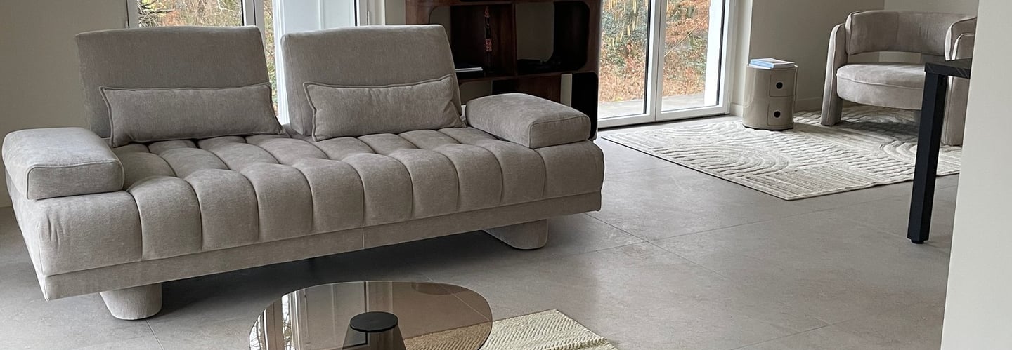 Salon moderne avec un canapé beige capitonné à rainures, des tables basses en verre