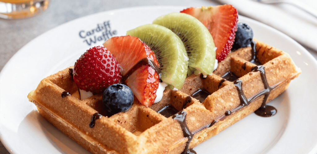 A close-up of a golden waffle topped with fresh strawberries and drizzled with rich Belgian chocolate sauce.