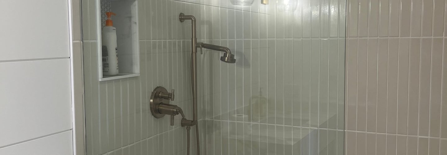 Modern walk-in shower featuring gold fixtures, vertical subway tile, and a glass partition wall.