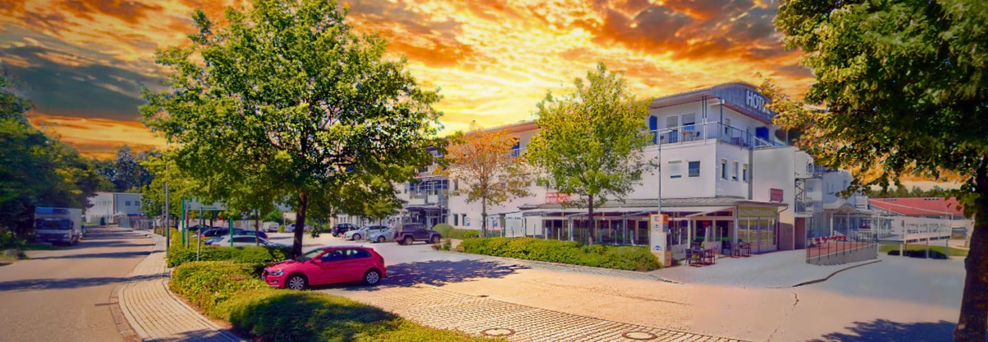 Modern white hotel building and parking lot under a vibrant orange sunset sky.