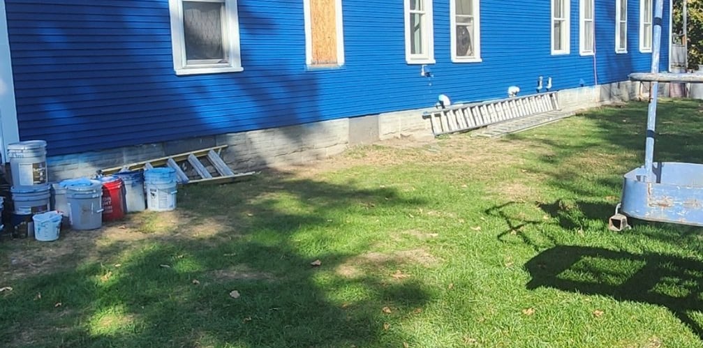 A vibrant blue house with white trim, surrounded by painting supplies, suggests a recent or ongoing exterior home renovation